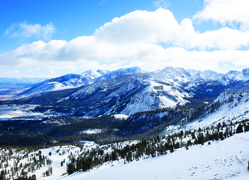 A view of snowy mountains and puffy clouds on a sunny winter day in Mammoth Lakes, California.