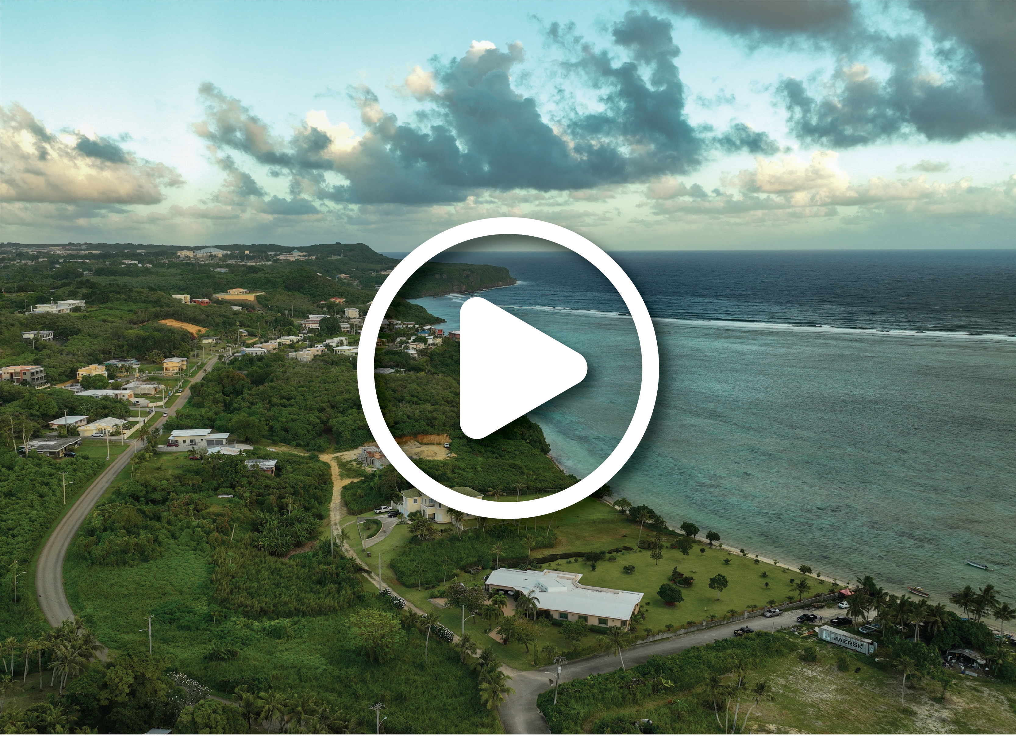 Coastline in Guam. Teals and ocean blue contrast against the vibrant green landscape/ There are buildings scattered throughout this landscape.