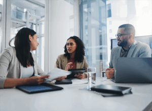 Three folks sit in a meeting discussing professional things.