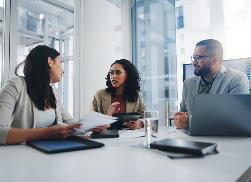 Three folks sit in a meeting discussing professional things.