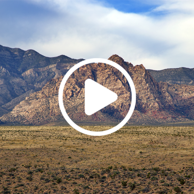 Video play button overlayed on Nevada landscape background, there is beautiful mountains with the dessert landscape and baby blue sky