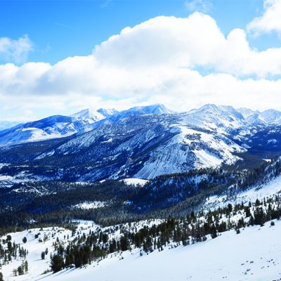 A view of snowy mountains and puffy clouds on a sunny winter day in Mammoth Lakes, California.